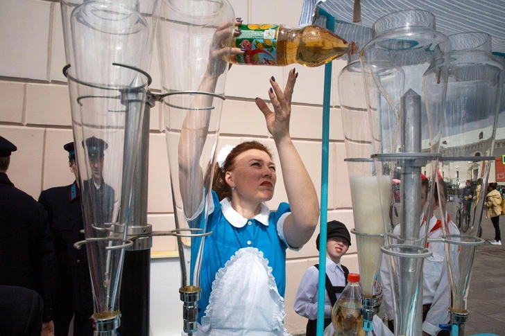 Продавщица разливает газировку в стеклянные емкости в советском уличном киоске, торгующем водой 1930-1940-х годов. На улице перед входом на станцию «Парк культуры» воссоздана церемония запуска первой в истории станции линии в 1935 году | Источник: Nikolay Vinokurov / Alamy via Legion Media
