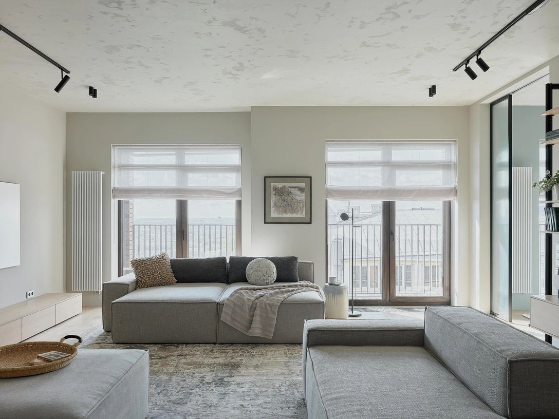 Кухня-гостиная. Помещение светлое за счет трех окон; дизайнеры стремились сохранить легкость и свет и не стали перегружать его отделкой. Мотив реки поддерживает декоративная штукатурка на потолке, ее рельеф напоминает блики на воде, особенно заметные в солнечный день. Диванная группа сделана на заказ в компании «Мистер Лаундж». Тумба и панель за тв — в компании «Аэлита». Текстиль — студия «Колобок». Торшер и общий свет, Maytoni. Ковер Kover.ru. Графика — Анна Лагеда. | Источник: Юрий Прокофьев. Стиль: Екатерина Шульц