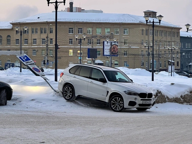 Автомобиль BMW X5 прижимает задним бампером столб со знаками парковки и стоянки. | Источник: читательница НГС