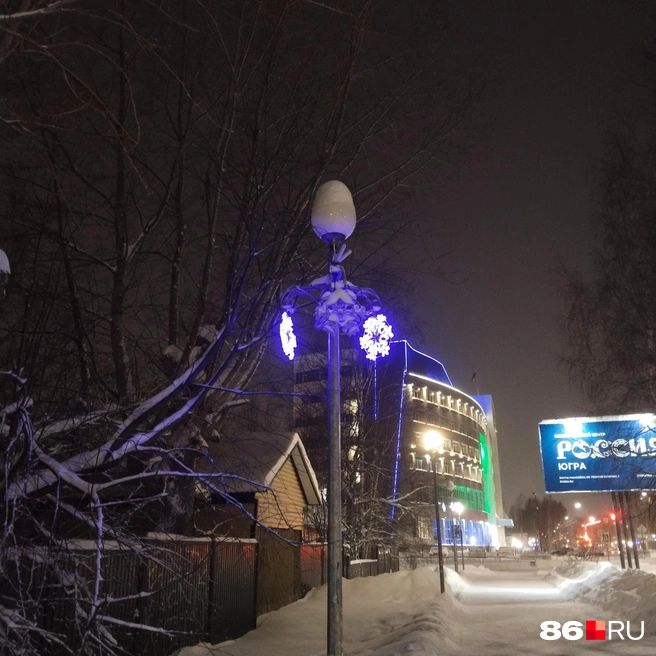 Еще на фонарях появились вот такие снежники. Некоторые синие, некоторые белые. Позади стенд, сообщающий об открытии филиала Национального центра «Россия»&nbsp;— большое событие для нашего города | Источник: Сабина Сафронова / 86.RU