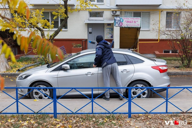 Мужчина изучает следы ночного происшествия, оставленные на лакокрасочном покрытии и сметает оставшиеся битые стекла | Источник: Алексей Волхонский / V1.RU