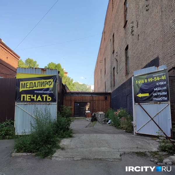 Яркая реклама на раскуроченных воротах, а впереди странное административное здание с бетонными плитами и столом | Источник: Ксения Власова / «ИрСити»