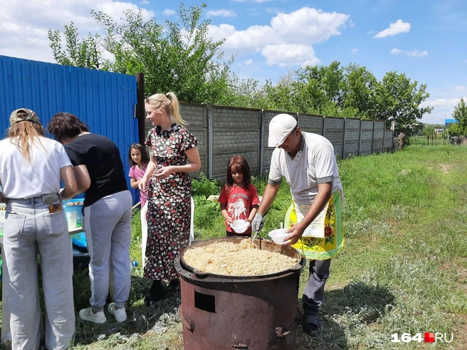 Повар Мирза заботливо раскладывал плов по тарелкам, а на столе к дополнению к плову стояли банки с солеными огурцами и арбузами. | Источник: Сергей Гендин / 164.RU