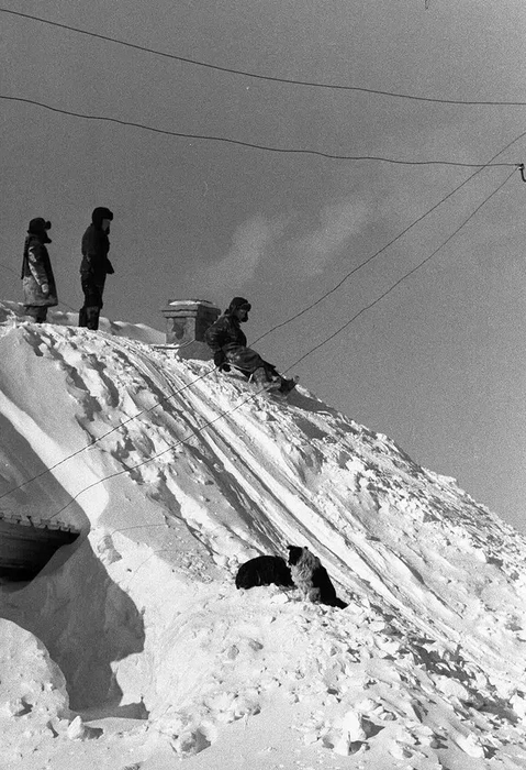 У ребятни горки были поскромнее. Некоторые из них появлялись на крышах домов, которые завалило снегом, как, например, в поселке Ижморском | Источник: Эдвард Хакимов / pastvu.com