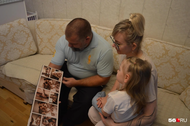 Михаил и Марина показывают семейный альбом, а на руках сидит младшая Михалина | Источник: Анастасия Баринова / 56.RU