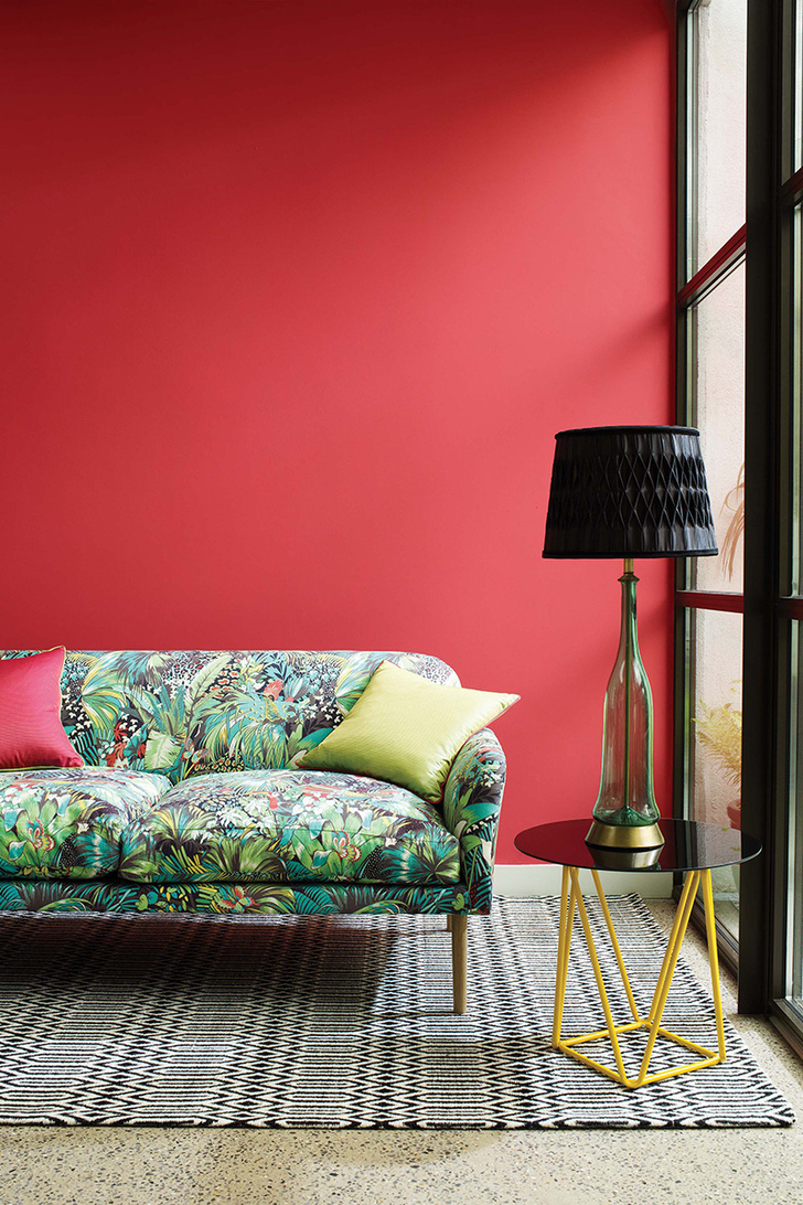 Сделать интерьер динамичным, можно выкрасив одну из стен в комнате в красный цвет. Диван в обивке тканью от Osborne & Little