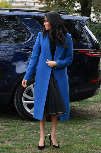 Накидка Пальто ─ настоящее спасение для Меган. Это ─ плотное, яркого синего оттенка и длины миди от канадского бренда SMYTHE полностью скрыло талию герцогини от посторонних глаз. Дело происходило на презентации специальной благотворительной книги рецептов, и все как-то подзабыли, что мама Меган, Дория Рэгланд, сопровождавшая ее на мероприятии, накануне приезда в Лондон посещала курсы по уходу за младенцами.