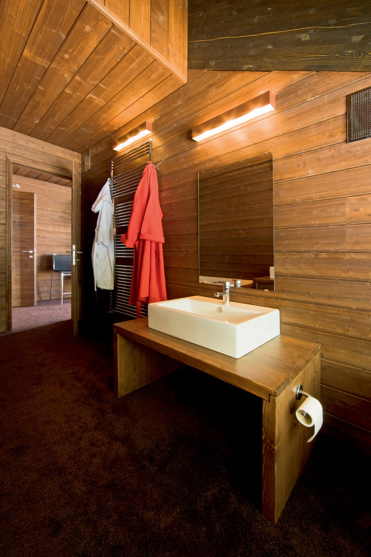 Стены ванной комнаты обшиты еловыми досками. На деревянном подстолье установлена раковина Fuori Box от Artceram со смесителем Lineare от Grohe. На стене — светильники Box от Oty Light.