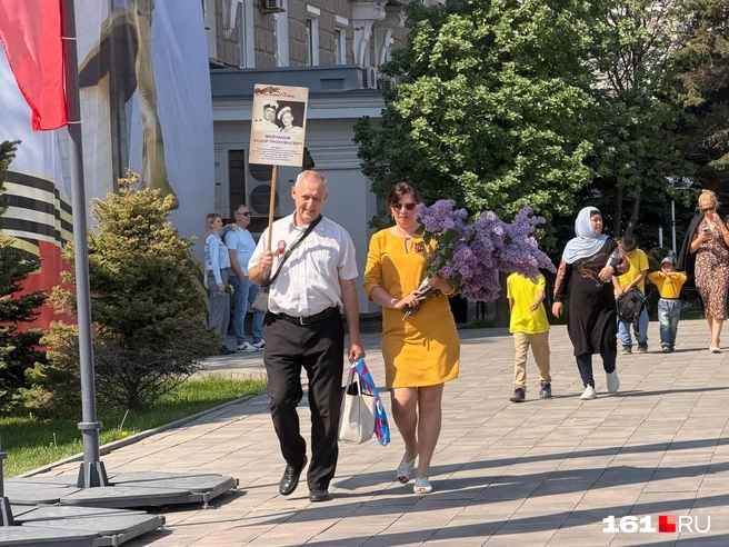 Горожане несут цветы к стеле и плакат с изображением ветеранов-родственников | Источник: Евгений Вдовин / 161.RU