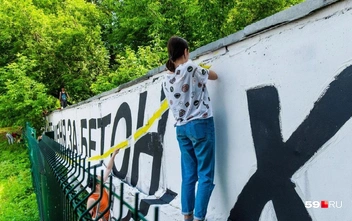 Девушке пришлось залезть за забор-сетку, чтобы расписывать бетонный  | Источник: Тимофей Калмаков / 59.RU