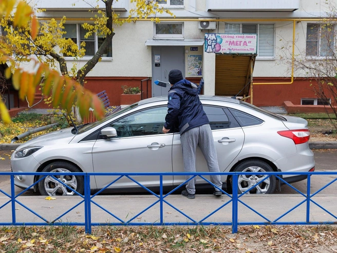 Мужчина осматривает повреждения на автомобиле и убирает осколки стекла | Источник: Алексей Волхонский / V1.RU