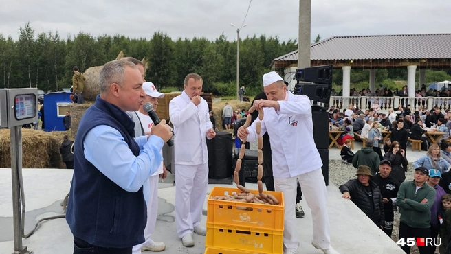 Александр Ильтяков показывает зрителям, какая колбаса получилась, которую коптили на костре | Источник: Дарья Никитченко / 45.RU