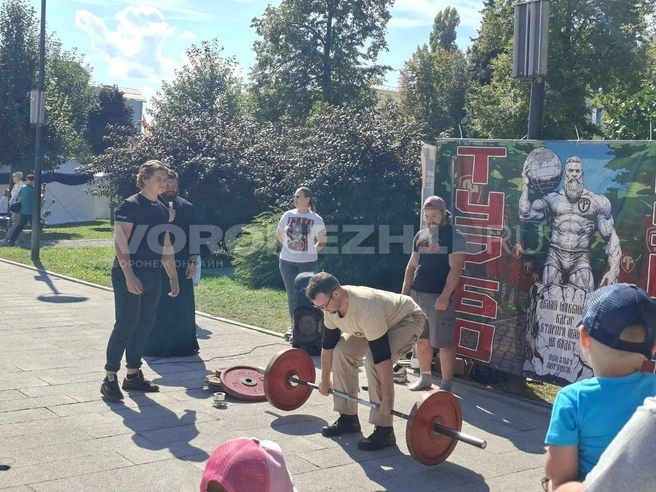 Отец Алексий (слева с микрофоном) наблюдает за попытками воронежцев поднять штангу | Источник: Алёна Воропаева / Voronezh1.ru