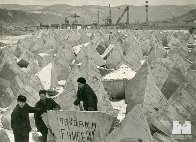 Начало 1963 года. Бетонные тетраэдры, заготовленные к перекрытию. На скале — ответ глыбе 1959-го: «Покорим Енисей!» | Источник: Красноярский краевой краеведческий музей / Vk.com