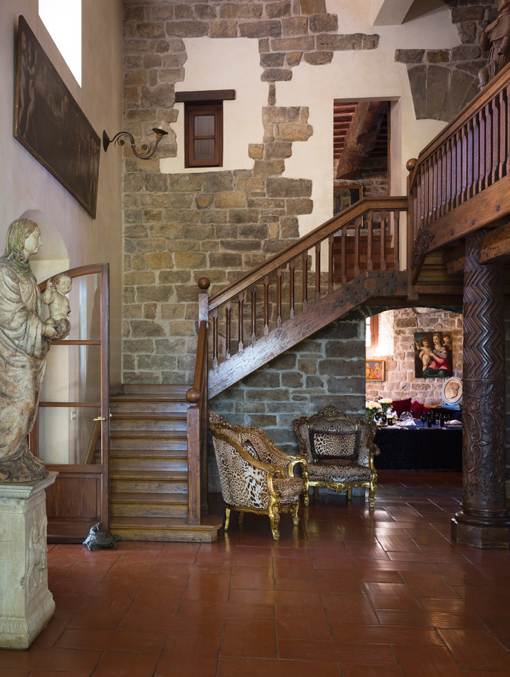 Старая лестница ведет на второй этаж, где находятся спальни. Полы выложены керамической плиткой. Кресла в «хищной» обивке, Roberto Cavalli Home.