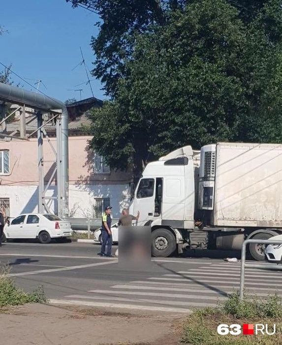 Водитель большегруза общается с госавтоинспектором, а мужчина с рваными ранами ног лежит под колесами | Источник: читатель 63.RU