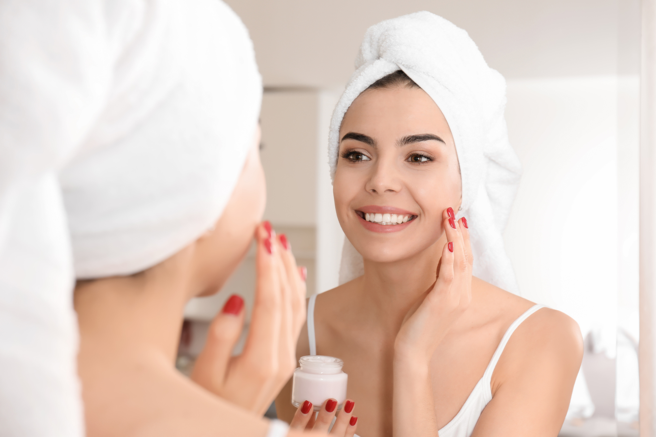 Happy young woman applying Cream onto face in Bathroom фото