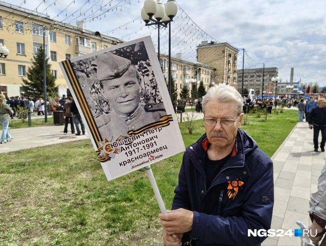 Пожилой красноярец рядом с фото своего отца | Источник: Геннадий Денисов / NGS24.RU