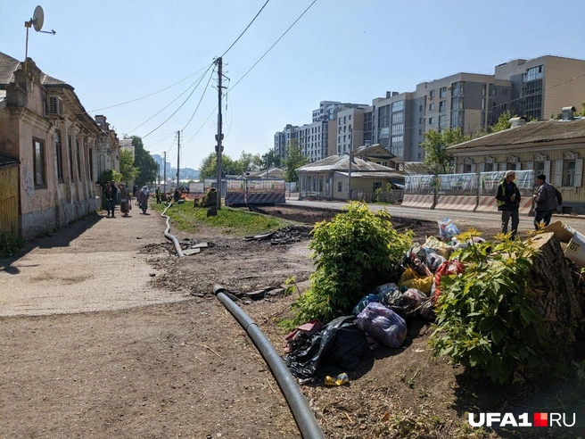 Повсюду мешки с мусором, снятый асфальт и трубы. На участке снуют рабочие и гуляют местные жители