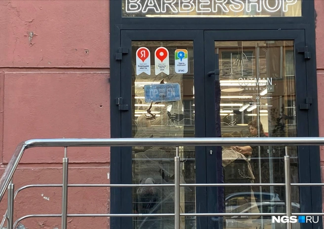 Необычные украшения к Хэллоуину появились и у мужской парикмахерской на улице Урицкого. На входной двери барбершопа развесили искусственную паутину, а на стекло наклеили изображения с летучими мышами и руками | Источник: Анастасия Хрипушина/NGS.RU