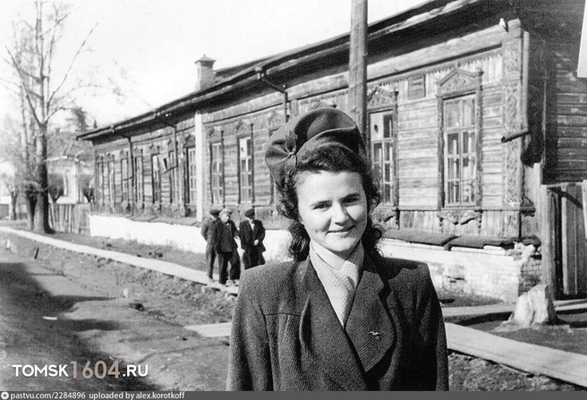 Красавица с ямочками на фоне деревяного дома на улице Кузнецова. Волосы девушки уложены, а украшает ее голову объемная шапка с бантиком. Есть ощущение, что пальто на томичке из прошлого отлично вписалось бы в современную моду (1945–1960 гг.) | Источник: pastvu.com