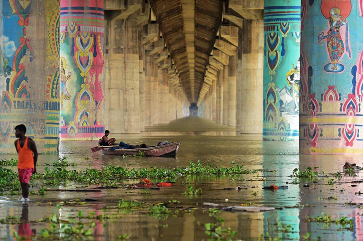 Житель Индии плывет на лодке под мостом