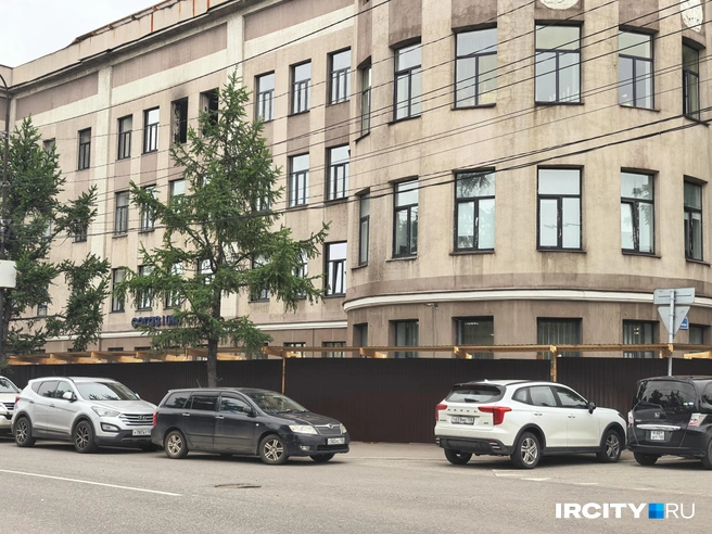 Часть территории здания со стороны повреждённых этажей огородили забором из профлиста. | Источник: Алёна Кашпарова / «ИрСити»